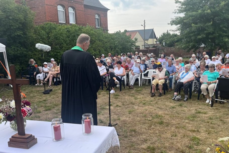 Frau mit Kreuz und Tisch, im Hintergrund Musiker mit Instrumenten.