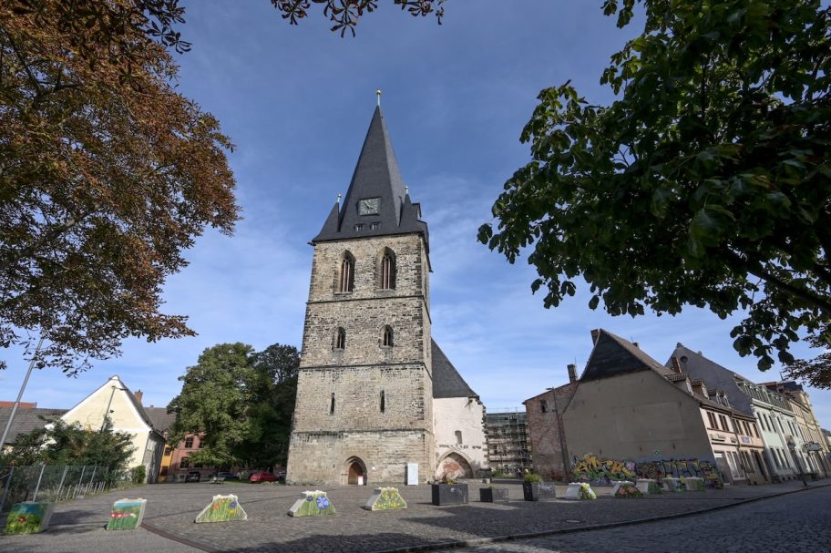 Historisches Gebäude mit einem hohen Turm und umgebenden Bäumen und Häusern.