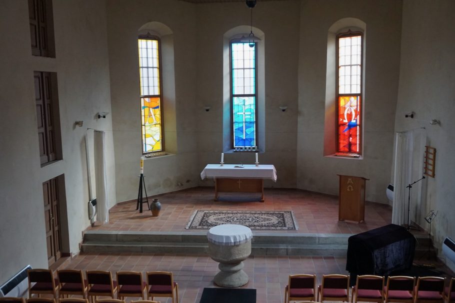 Helle Innenansicht einer Kirche mit bunten Fenster und einem Altar.