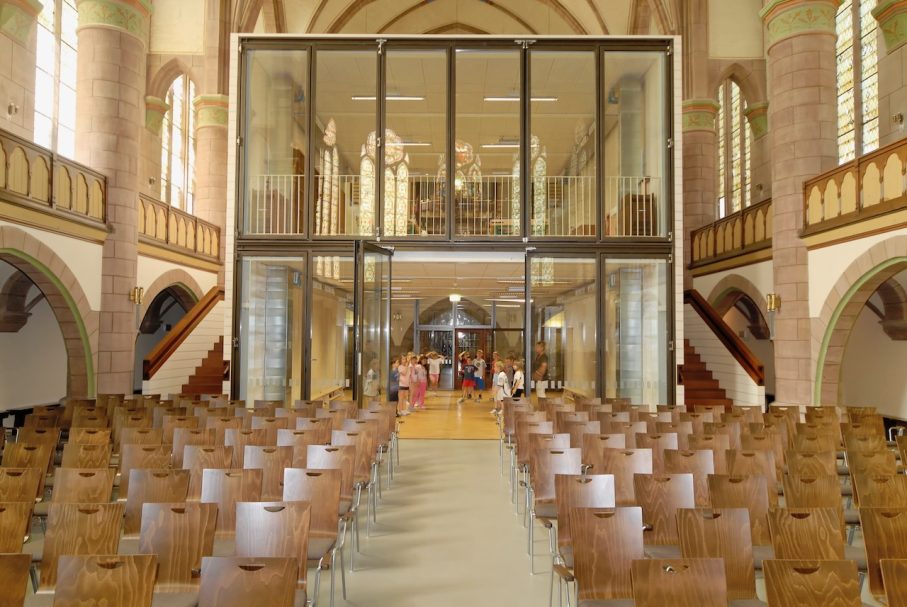 Moderne Zusatzstruktur in einem historischen Kirchenraum mit Sitzreihen.