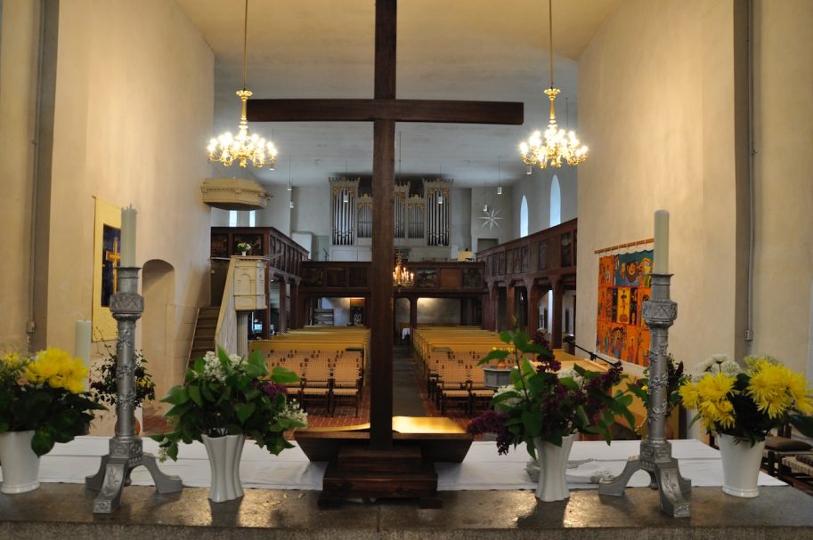 Altar mit Holz-Kreuz, Blumenarrangements und Kerzen in einer kirchlichen Umgebung.