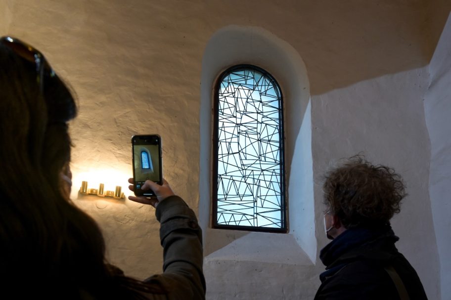Eine Person fotografiert ein farbiges Fenster in einem historischen Raum.