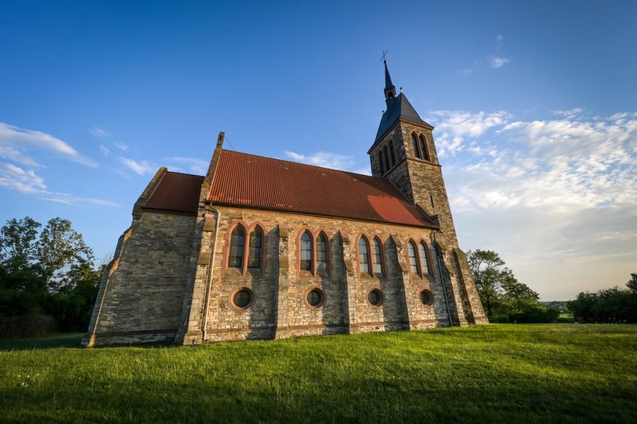 Eine alte Kirche mit einem spitzen Turm und bunten Fenstern, umgeben von Wiese.