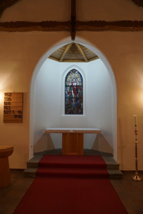 Kapelle mit rotem Teppich, Holzdecke und einem farbigen Glasfenster.