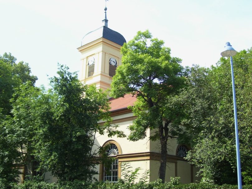 Historisches Gebäude mit Uhrturm, umgeben von Bäumen und Grünanlagen.