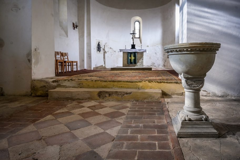 Innenansicht einer kleinen Kapelle mit Altar und Taufbecken aus Stein.