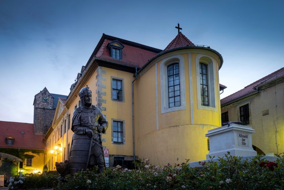 Gelbes Gebäude mit Statue und Laternen, bei Dämmerung beleuchtet.