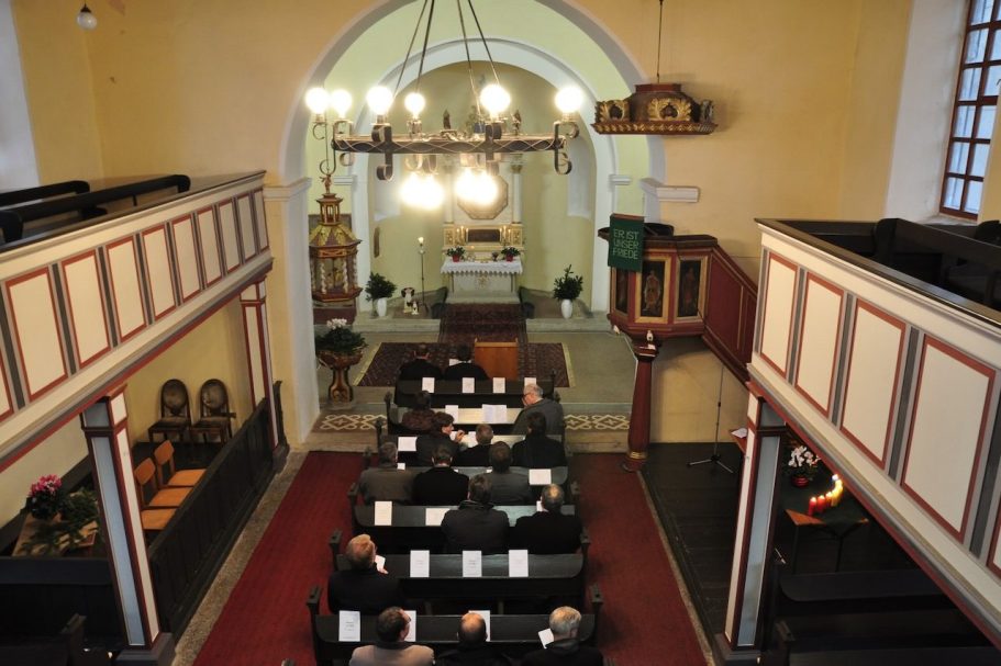 Frau mit Kreuz und Tisch, im Hintergrund Musiker mit Instrumenten.