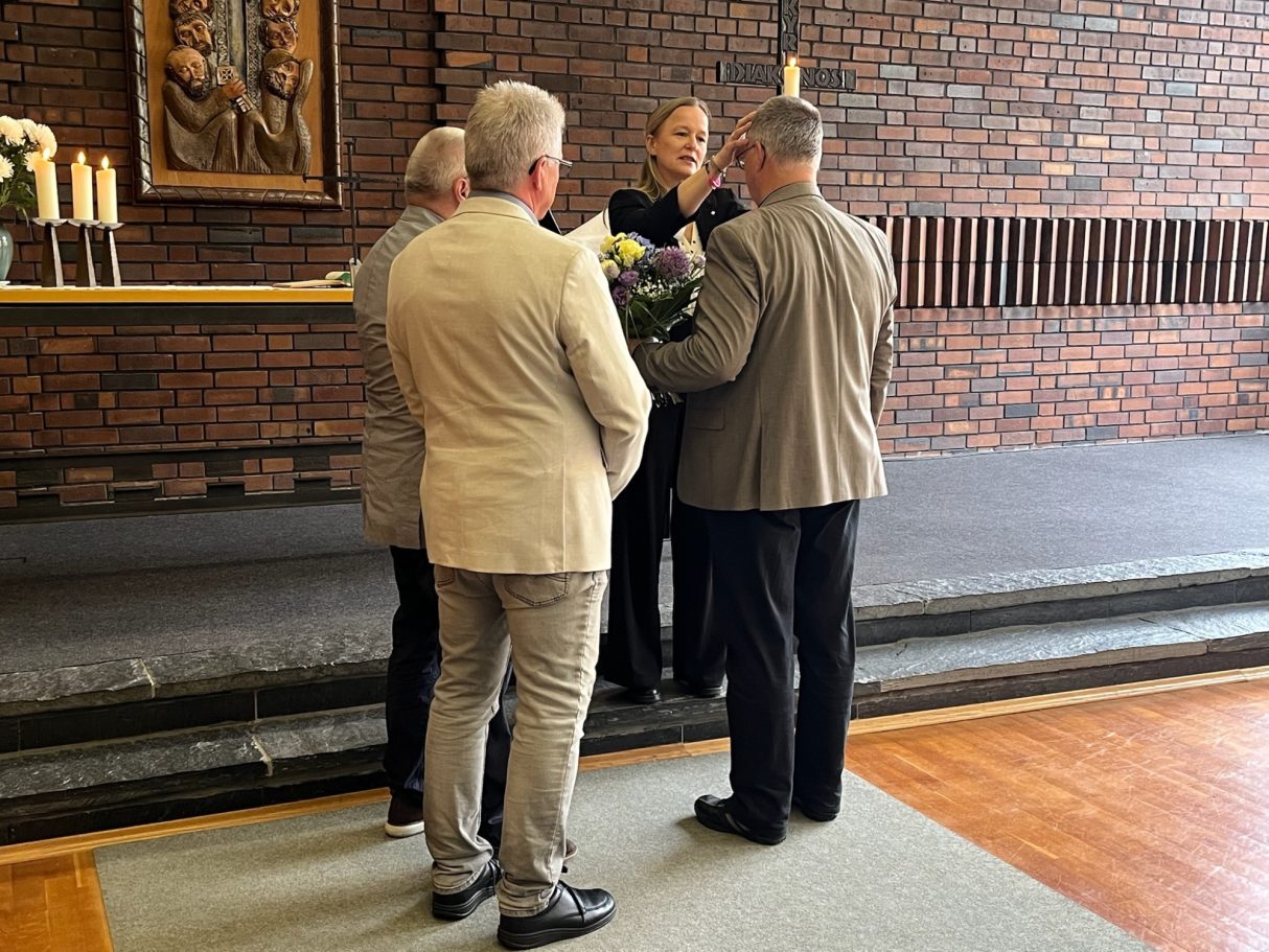 Vier Personen stehen in einem Raum und sprechen mit einer Frau, die Blumen hält.