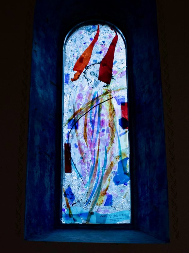 Buntes Kirchenfenster mit einer stilisierten Gestalt in hellen Farben.
