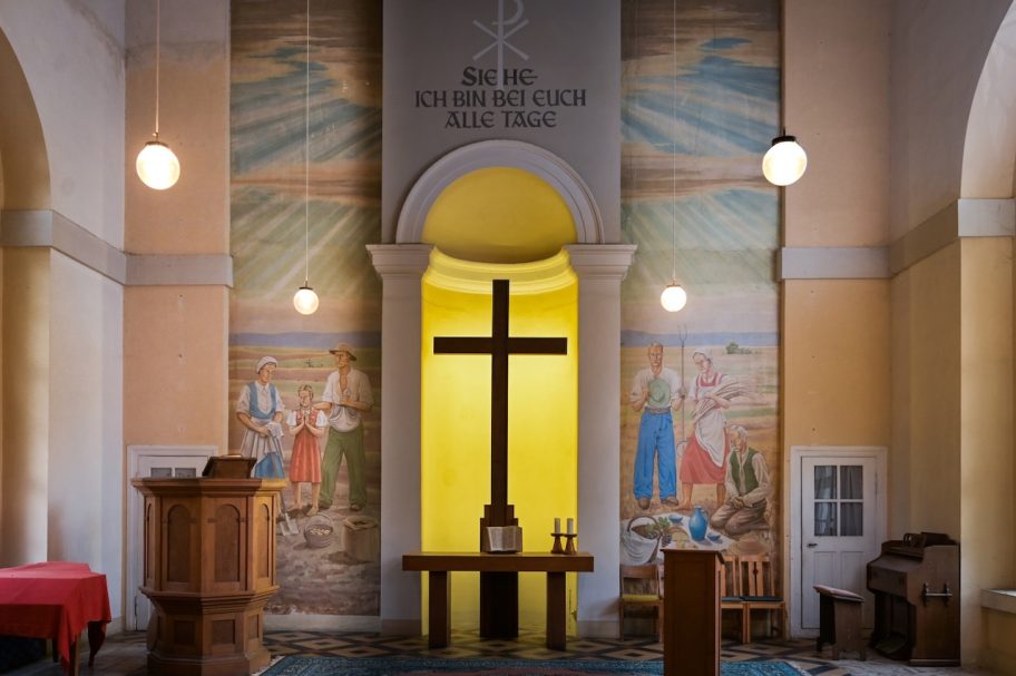 Holzkreuz in einer Kirche mit bunten Wandmalereien im Hintergrund.