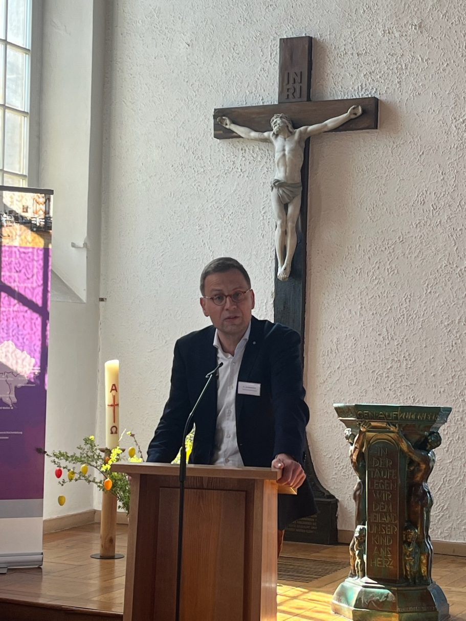 Mann spricht an einem Podium vor einem Kreuz in einer Kirche.