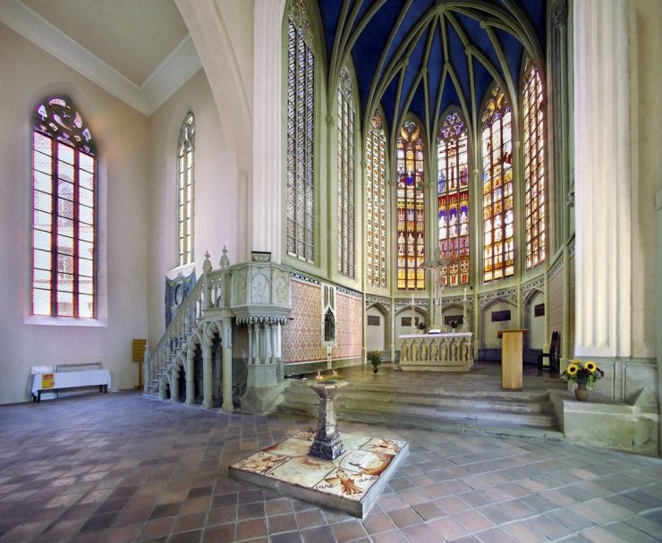 Innenansicht einer Kirche mit hohen Fenstern und einem dekorativen Altar.