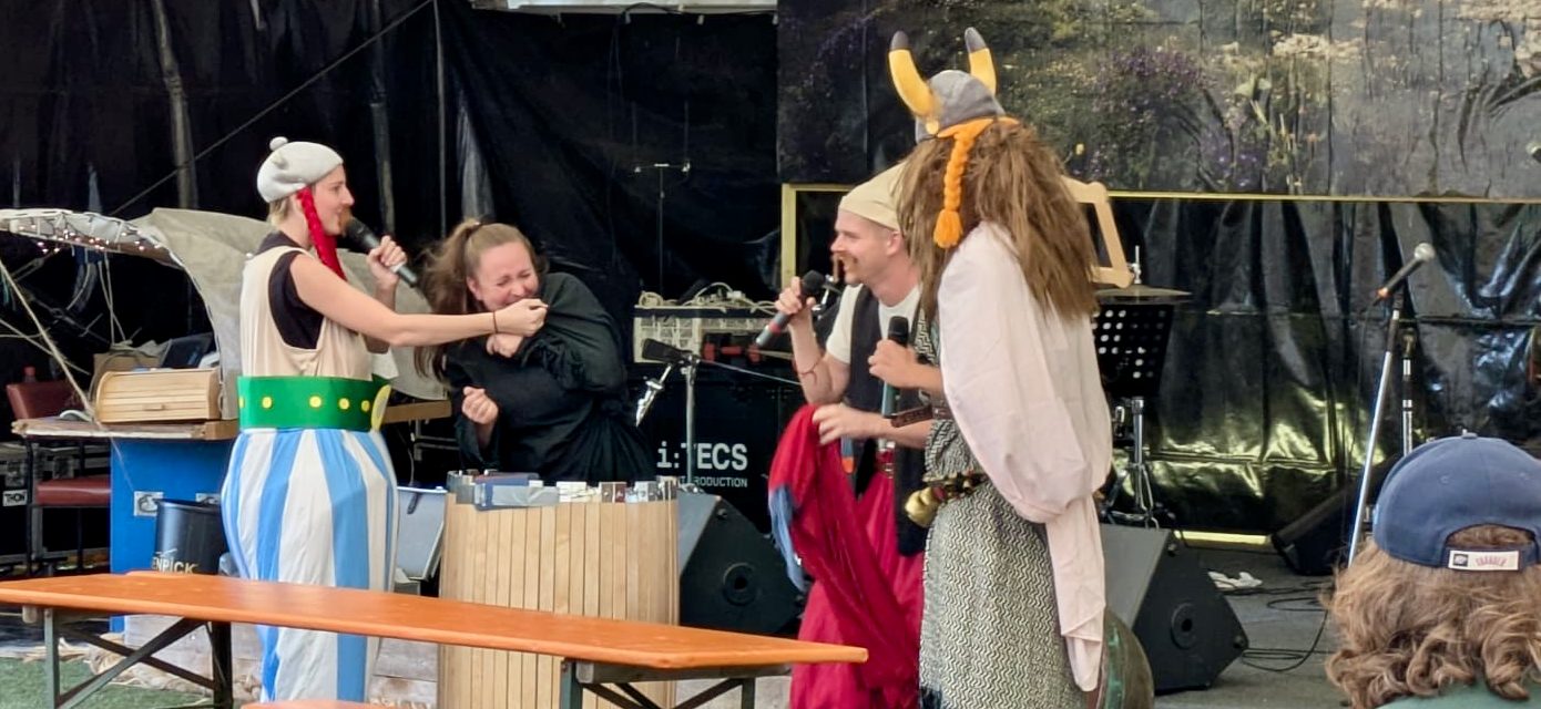 Proben einer Theateraufführung mit Schauspielern und Musiker:innen auf der Bühne.