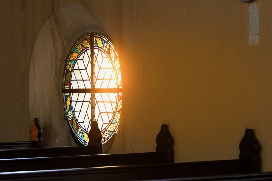 Buntglasfenster mit Sonnenlicht, das auf Bänke in einer Kirche fällt.